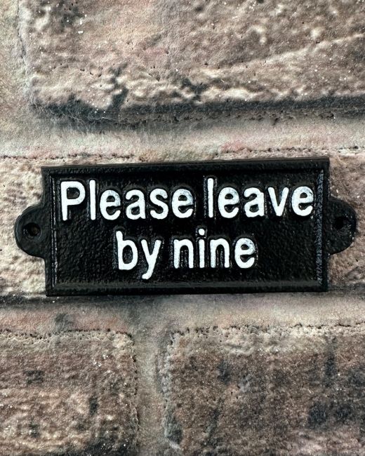 "Please Leave by Nine" Traditional Cast Iron Wall Sign mounted on a brick wall