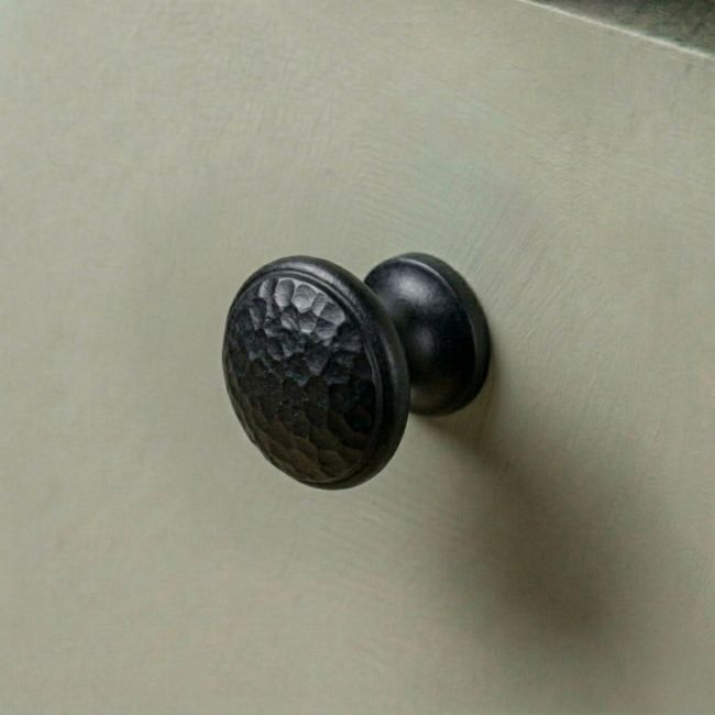 A 30mm Black Hammered Iron Cabinet Knob Mounted on a Light Green Kitchen Cupboard - Digital Illustration 