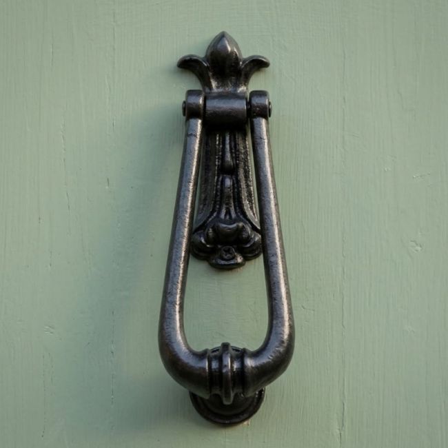 A Traditional Black Malleable Iron "Millingdale Court" Door Knocker Shown up close on a Green Timber Door - Digital Illustration