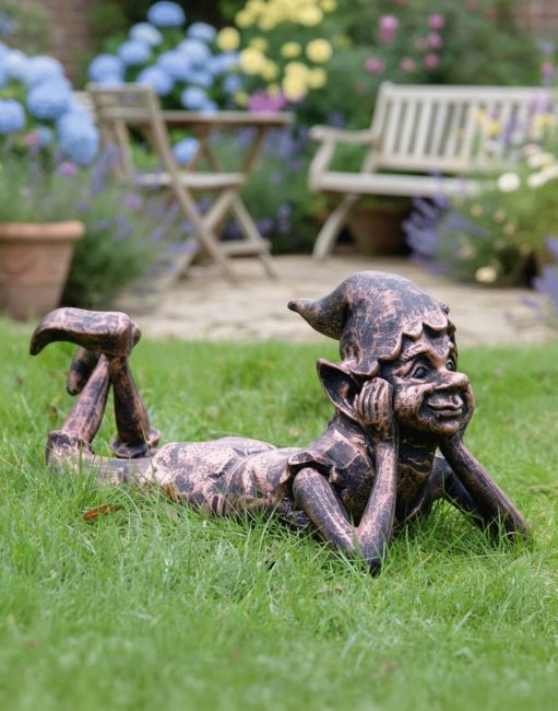 Digital Illustration of the "Reverie" the Copper Version of the Pixie Cast Aluminium Garden Sculpture Lying on a Traditional Grass lawn in Front of Garden Furniture