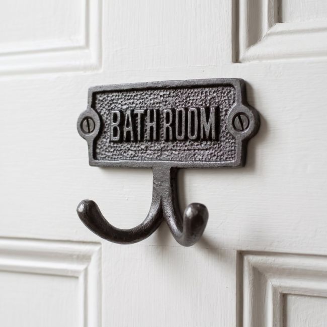 The Bathroom Plaque Double Robe Hook in Cast Antique Iron Shown Mounted onto the Back of a white Door - Digital Illustration