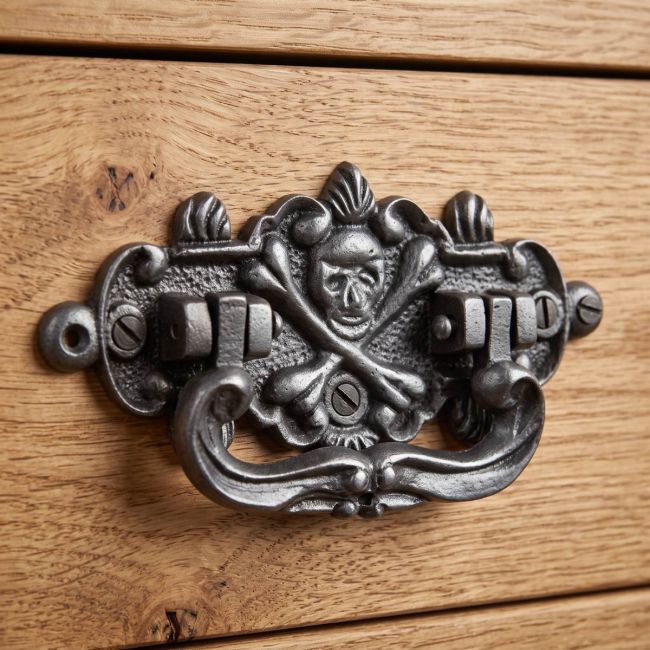 The Cast Antique Iron Skull & Crossbones Drop Handle - Antique Iron Finish Shown on a Wooden Drawer - Digital Illustration