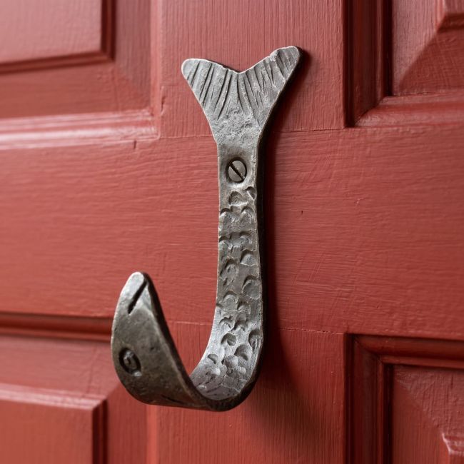 The Hand-Forged Fish Single Coat Hook - 110mm Mounted onto a Red Door Shown Close up - Digital Illustration