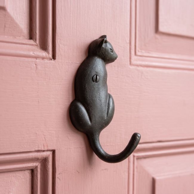 The Seated Cat Antique Iron Coat Hook - 125mm Shown Mounted on the Back of a Pink Door - Digital Illustration