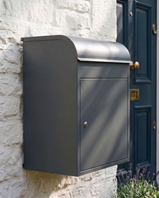 The "Titan" Medium Wall Mounted Parcel Box Steel in Grey Shown Mounted to a White Wall on a Country Garden Home - Digital Illustration