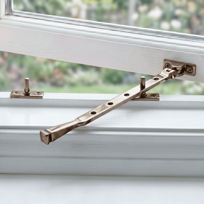 The 12" Polished Bronze Window Stay Mounted on an Open White Window in a Contemporary Home - Digital Illustration