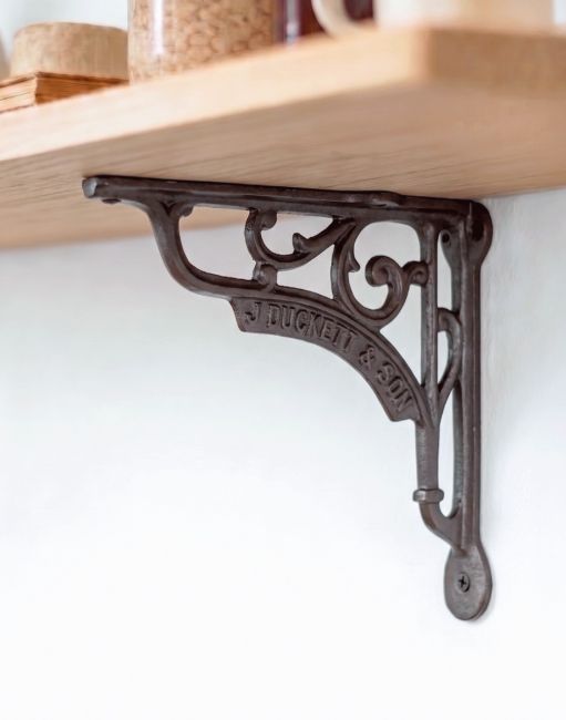 The 18 x 20cm "J Duckett & Son" Iron Bracket Used to Mount a Wooden Shelf on a White Modern Kitchen Wall - Digital Illustration