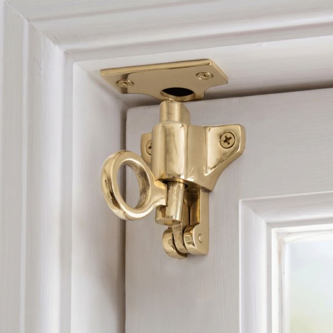 The "Atwood" Polished Brass Fanlight Catch with Two Keeps Attached to a White Door and Door Frame in a Contemporary Home Interior - Digital Illustration 