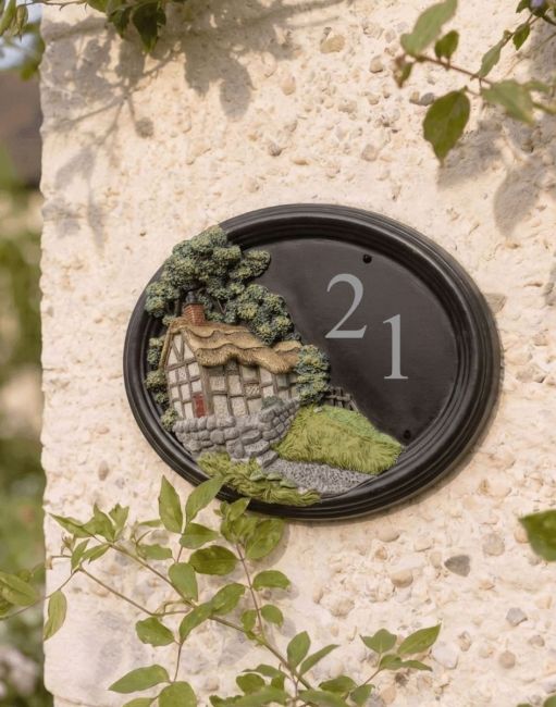 A Number 122 "Avenbury Thatch" Hillside Cottage Oval House Sign Mounted on a Cream Coloured Cottage Garden Wall - Digital Illustration A Number 122 "Avenbury Thatch" Hillside Cottage Oval House Sign Mounted on a Cream Coloured Cottage Garden Wall - Digital Illustration