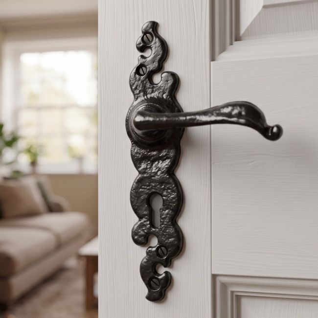 The "Helmford" Slim Black Ornate Iron Door Handles on a Grey door that Leads to a Living Room - Digital Illustration 