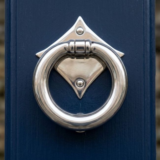 The "Lorien" Ring Door Knocker - Polished Stainless Steel on a Dark Blue Front Door on a Sunny Day - Digital Illustration 