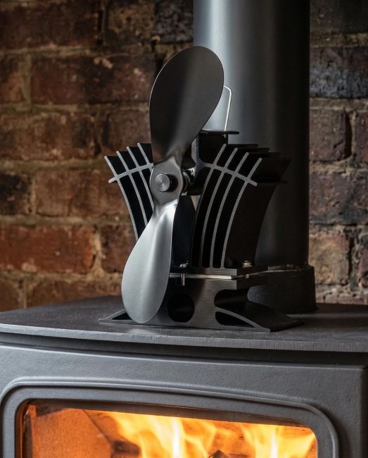 The 24cm Black "BelAir" Eco Wood Stove Fan Next to a Log Pile inside a Country Home Fireplace - Digital Illustration