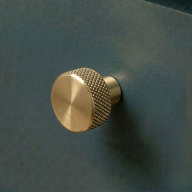 The 25mm "Vesper" Knurled Edge Cabinet Knob in Aged Brass Designed for Kitchen Cupboards Mounted on a Blue Drawer - Digital Illustration 