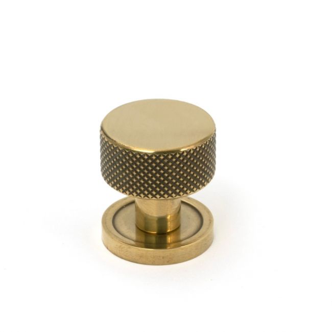 The 25mm Knurled Cabinet Knob on a Plain Rose in Aged Brass Shown Upright on a White Background The 25mm Knurled Cabinet Knob on a Plain Rose in Aged Brass Shown Upright on a White Background