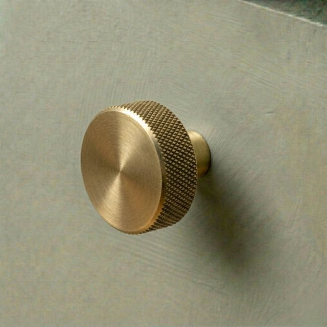 The 38mm "Vesper" Knurled Edge Cabinet Knob in Aged Brass Designed for Kitchen Cupboards Displayed on a Green Drawer - Digital Illustration