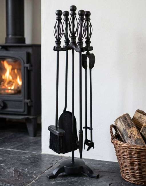 The 66cm Classic Black Iron Companion Set with Basket Handles next to a Traditional Log Burner Stove - Digital Illustration