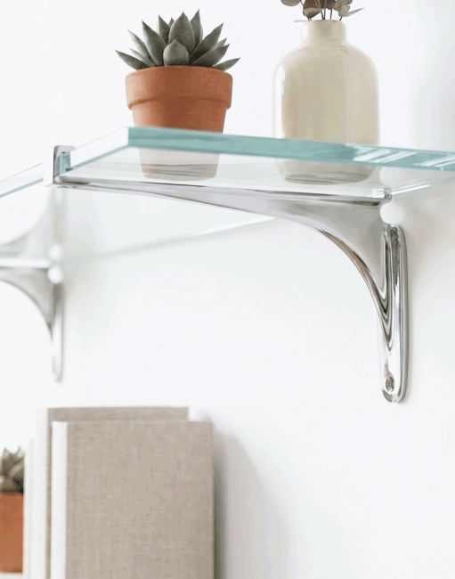 The 9cm x 18cm Kelsall" Bright Chrome Glass Shelf Bracket Mounted on a White Wall in a Modern Living Room - Digital Illustration