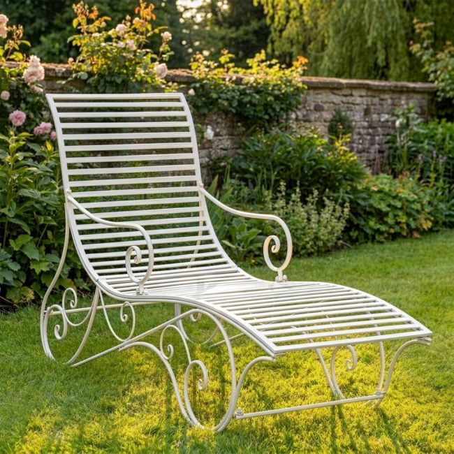 The "Windsor" Scrollwork Wrought Iron Sun Lounger in a Cream Finish Positioned on a Sunny Garden Lawn - Digital Illustration 