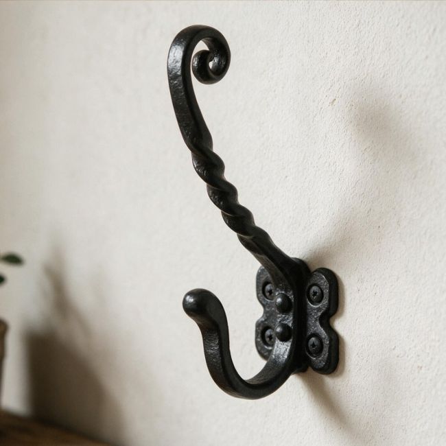The Black Antique Iron Monkey Tail Twist Design Wall Coat and Hat Hook on a White Wall next to a Timber Shelf - Digital Illustration The Black Antique Iron Monkey Tail Twist Design Wall Coat and Hat Hook on a White Wall next to a Timber Shelf - Digital Illustration