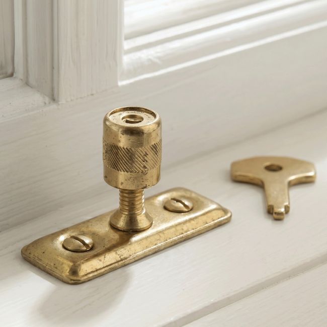 The Casement Stay Locking Pin in Front of a Wooden Window Frame in a Country Home in a Gold Plated Finish - Digital Illustration
