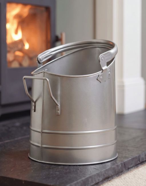 The Pewter Finish Traditional Fireside Log and Coal Bucket In Front of a Lit Fireplace in a Contemporary Home - Digital Illustration