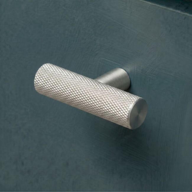 The Aged Brass "Astor" Knurled Industrial T-Bar Cabinet Handle Mounted on a Dark Blue Kitchen Cupboard Drawer - Digital Illustration 