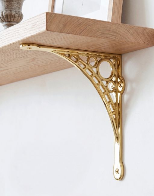 The Small 20cm x 22cm Polished Brass "Iron Bridge" Shelf Bracket Mounted on a Cream White Coloured Wall on a DIY Wooden Shelf - Digital Illustration 