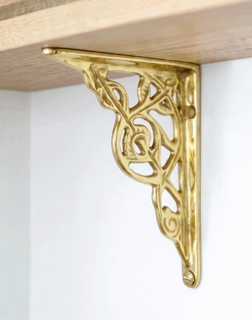 The Small Trellis Brass Shelf Bracketin Polished Brass Mounted on a White Coloured Modern Interior wall - Digital Illustration 