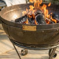 Digital Illustration of the 60cm Version of the Iron Kadai Bowl Fully Lit in Front of Rustic Garden Furniture Badge close Up Digital Illustration of the 60cm Version of the Iron Kadai Bowl Fully Lit in Front of Rustic Garden Furniture Badge close Up