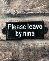 "Please Leave by Nine" Traditional Cast Iron Wall Sign mounted on a brick wall