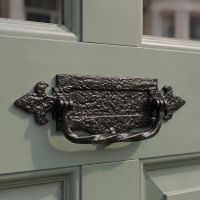 A 14" Antique Black Iron Fleur De Lys Door Letter Plate With Integral Knocker Fixed onto a Front Door of a Period Property - Digital Illustration