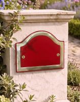 A Blank Arched House Number Plaque in a Claret & Brass Finish Mounted on a Driveway Wall.
