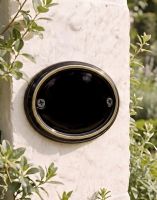 A Blank Brass & Black Oval House Number Plaque Mounted on a Sunny White Property Wall - Digital Illustration