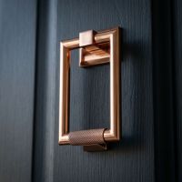 A Close up Image of the Modern Knurled Rectangular Door Knocker in Polished Bronze on a Blue Coloured Front Door - Digital Illustration