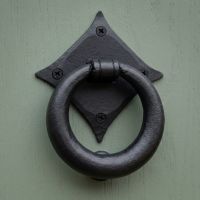 A close up of the Matte Black Iron Traditional Ring Door Knocker on a Sage Green Front Door - Digital Illustration 
