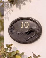 A Number 10 Greyhound House Number Sign in a Bronze Finish Mounted on a Cream Coloured Cottage Wall - Digital Illustration 