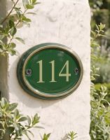 A Number 114 in Vinyl Polished Brass & Green Cast Oval House Number Sign Mounted on a Cream Coloured Building Wall - Digital Illustration