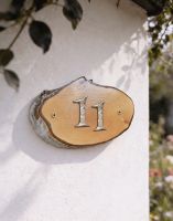 A Number 11 Natural Hard Wood Rustic House Number Sign Mounted on a Sunny White Cottage Wall - Digital Illustration 