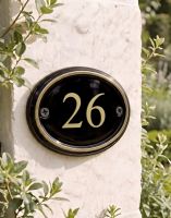A Number 26 in Vinyl Polished Brass & Black Oval House Number Sign Mounted on a Sunny White Building Wall - Digital Illustration A Number 26 in Vinyl Polished Brass & Black Oval House Number Sign Mounted on a Sunny White Building Wall - Digital Illustration