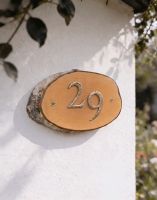 A Number 29 Natural Hard Wood Rustic House Number Sign Mounted on a Sunny White Cottage Wall - Digital Illustration