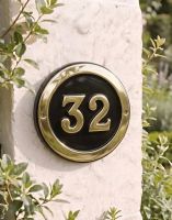 A Number 32 Round Brass & Black House Number Sign Mounted on a Textured Cottage Wall - Digital Illustration