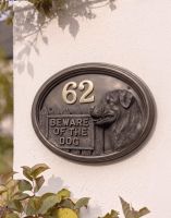 A Number 62 Rottweiller House Number Sign in a Bronze Finish Mounted on a Cream Coloured Cottage Wall - Digital Illustration 