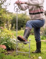 A Silver Boot Scraper Being Used Outside by a Gardener Next to a Flower Border - Digital Illustration