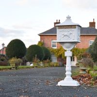 Classic White Freestanding Huntingdon Post Box with countryside house in background Classic White Freestanding Huntingdon Post Box with countryside house in background
