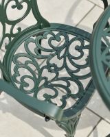 Close up of ornate seat detail in dark green garden two seater table and chairs set Close up of ornate seat detail in dark green garden two seater table and chairs set
