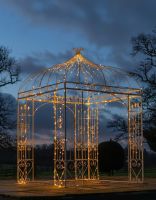Digital representation of Deluxe Wrought Iron "Annabella" Cream Powder Coated Gazebo lit up with fairy lights at night