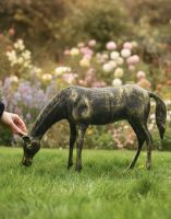 Digital illustration of Black and Gold Grazing Foal Garden Sculpture with hand in shot for scale