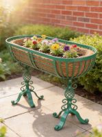 Digital Illustration of the Green "Highgate" Free Standing Trough Planter in Situ in the Garden Holding Colourful Flowers