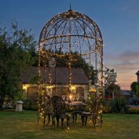 digital representation at night lit up with fairy lights Black ornate scroll gazebo in garden