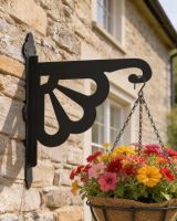 Digital representation of Clam Design Heavy Duty Iron Hanging Basket Bracket mounted on a farmhouse